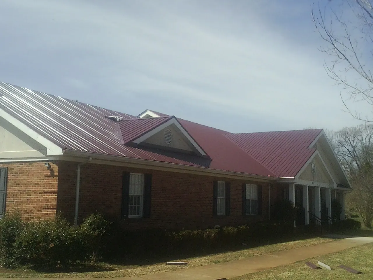 Red metal roof with gabled entries on a long brick building, from a Hail Damage Roof Repair job in West Covina