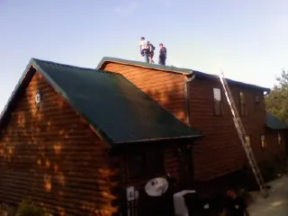 Crew on the ridge of a green metal roof on a two story log home in West Covina