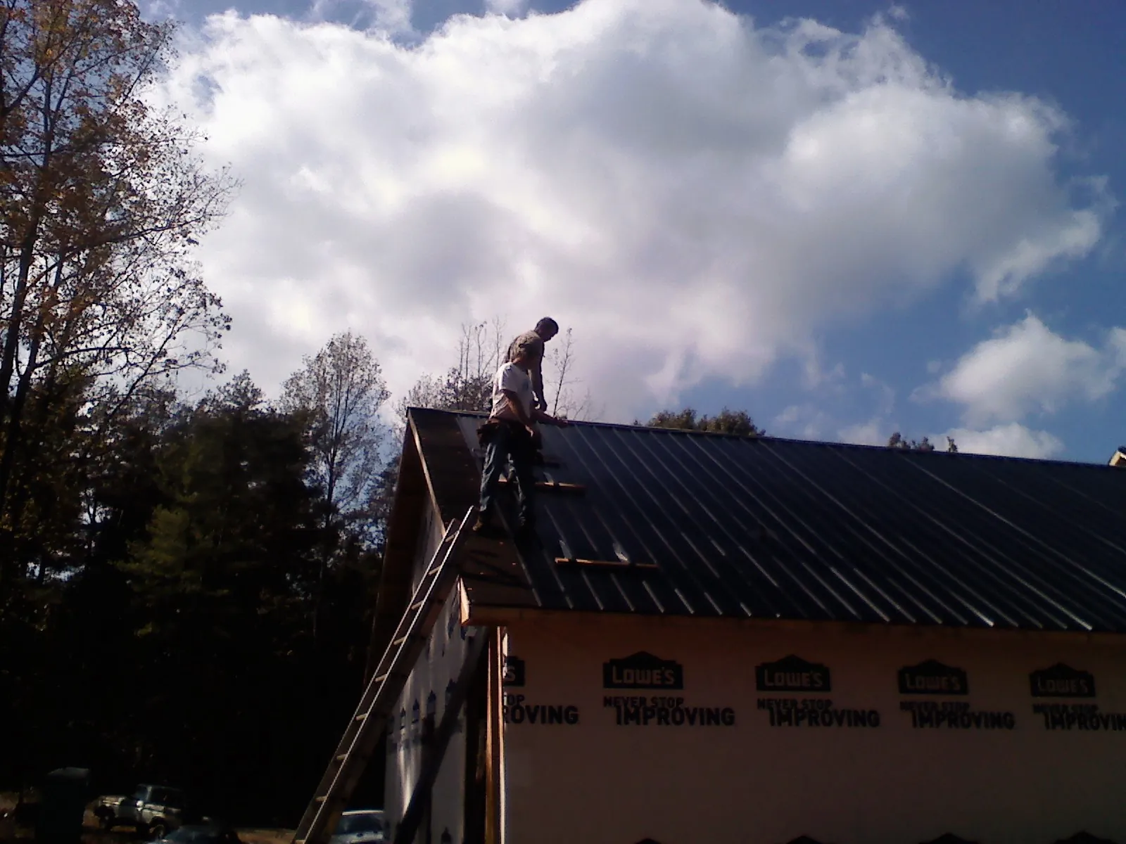 Roofer fastening dark metal panels high against a cloudy sky, from a Roof Inspection job in West Covina