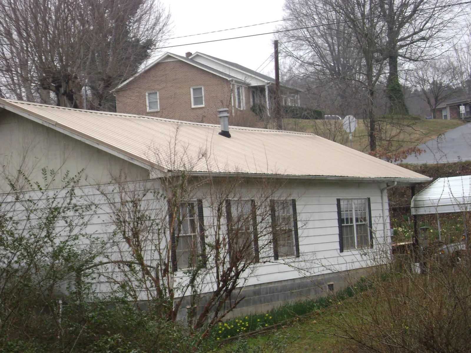 Tan metal roof on a white sided house set into a hillside — Commercial Roofing by Roofing Brothers in West Covina